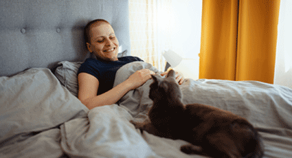 Cat sat on bed looking at woman sitting under covers
