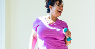 A smiling woman in a pink sports top excercising with hand weights 