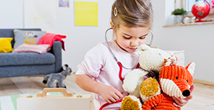 Young girl holding a stethoscope to her toys 310x160