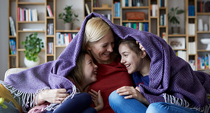 Woman under purple blanket with two children
