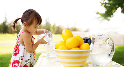 Young girl pouring water into a glass by a lbowl of melons, making lemonade