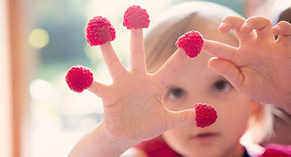Young girl with 5 raspberries, one on each finger
