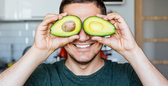 Man holding avocado halves up to his eyes