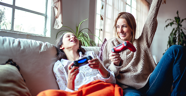 Mum and child laughing on the sofa holding video game controllers