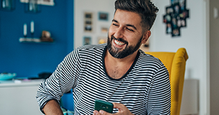 Man with beard and striped top holding his mobile whilst laughing