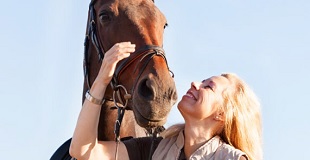 Blond woman looking up and smiling at her brown horse