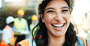 Woman in an orange hi-viz vest laughing whilst on a building site (blurred background)