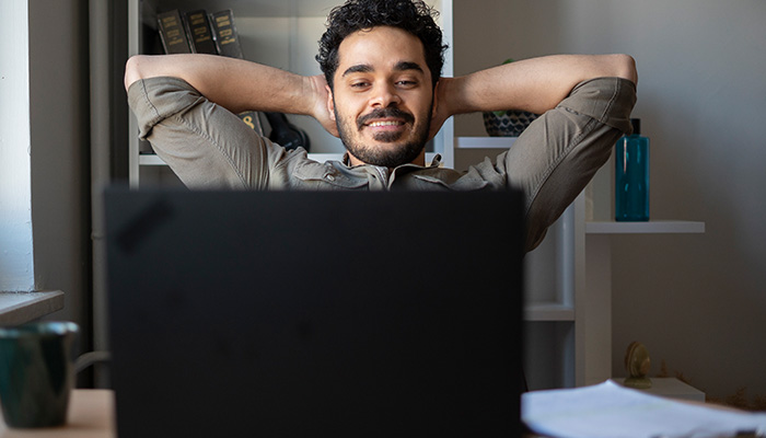 Young man relaxing in front of laptop smiling with his hands behind his head