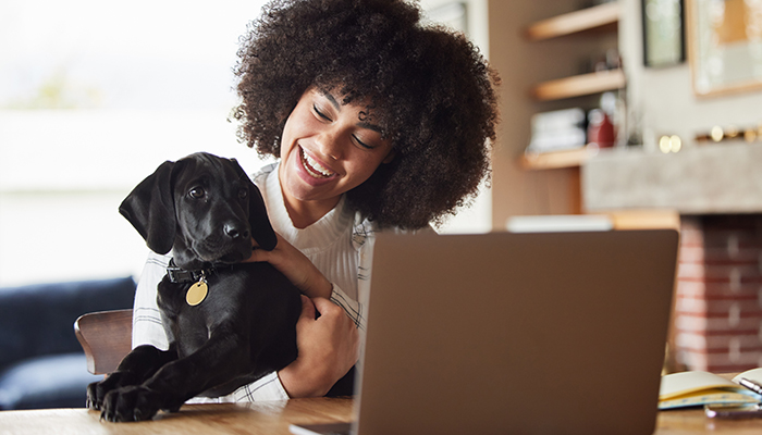 Smiling young women of colour holds her black labrador puppy in front of her open laptop