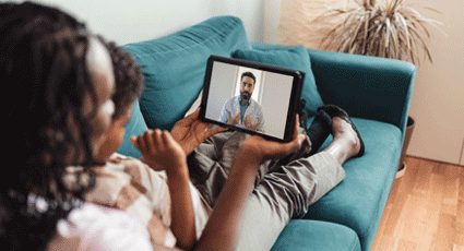 Woman sat on sofa looking at doctor on tablet