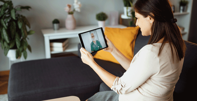 Woman sat on sofa looking at doctor on tablet