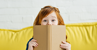 Young girl happily peeping over an open book