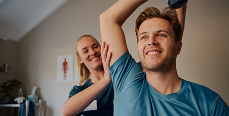 Female physio helping young male patient stretch his arm