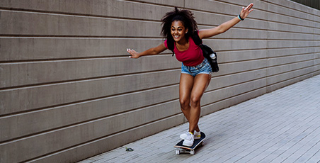 Young woman of colour, arms outstretched whilst riding a skateboard