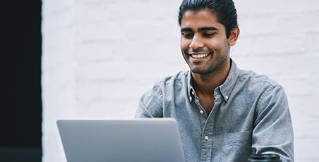 Young man of colour smiling whilst on a laptop