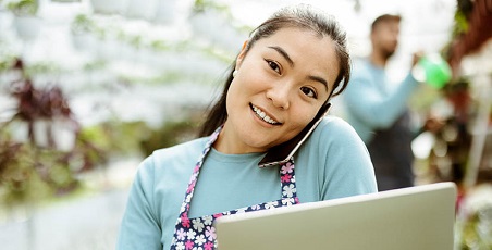 Young woman holding mobile phone to her ear whilst holding a laptop and smiling