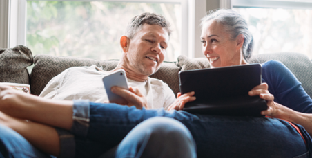 Middle-aged man and woman on sofa smiling at a tablet