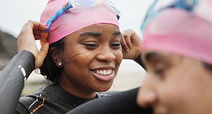 Two young women of colour smiling in wet suits and swimming caps