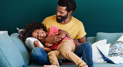 Young man of colour, playing with their child on sofa