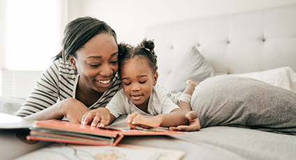 Young woman of colour and her daughter reading a story on a bed