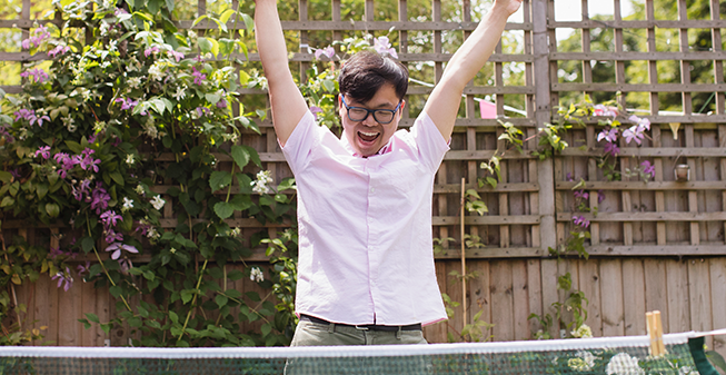 Young east asian man with glasses, celebrating winning at table tennis.
